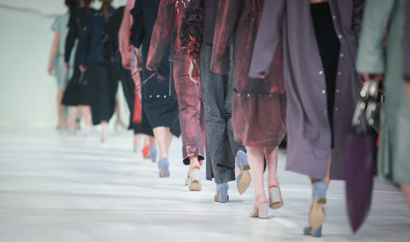 Models walking on a fashion show runway, away from the camera.