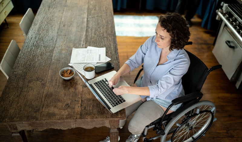 Woman in wheelchair working at a computer in a home.