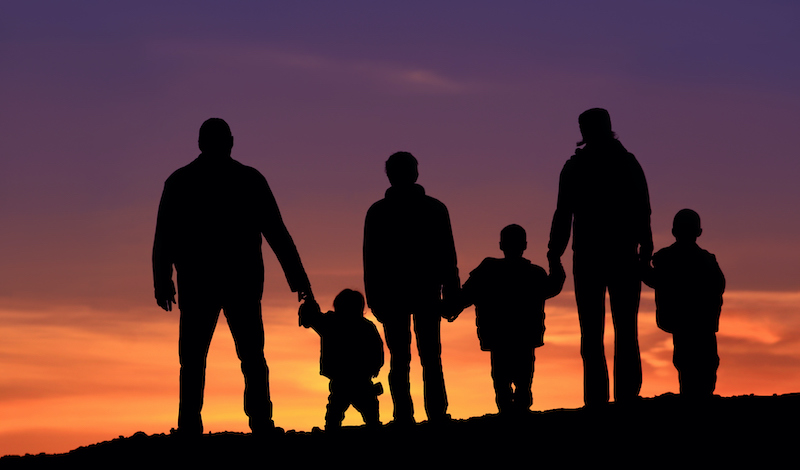 A silhoutte of a big happy family standing outside against dramatic sky. Two-generation family holding hands. Themes include bonding, love, relationships, togetherness, two parents, traditional family, father, mother, children, six people, four children, watching the sunset, back view, unrecognizable people.