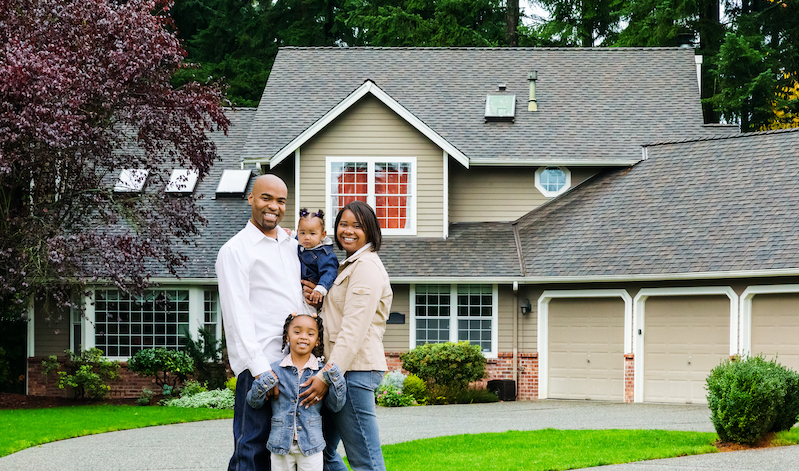 Black family of four standing in front of a home.